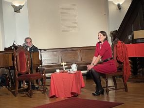 Szene eines Theaterstückes im Altarraum; Frau sitzt an einem gedeckten Teetisch und Mann am Klavier