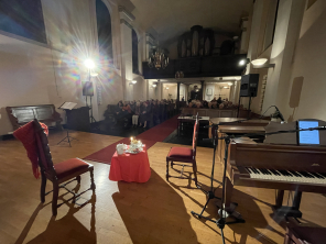 Bild in Richtung der Orgel in der Stadtkirche; volle Reihen an Zuschauern; Zu sehen ist der Aufbau der Szene (Teetisch und zwei Stühle)