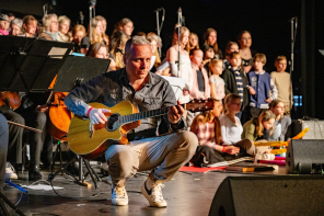 Musiker mit Gitarre kniet auf der Bühne