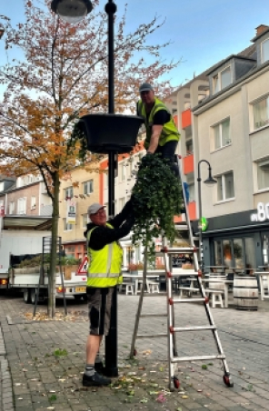 blumenampeln.jpg Männer bauen einen Blumenkasten an eine Ampel
