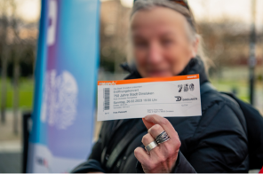 verschwommene Person, die ein Eintrittsticket in die Kamera hält. Sie steht vor einer Fahne im Design des Stadtjubiläums. verschwommene Person, die ein Eintrittsticket in die Kamera hält. Sie steht vor einer Fahne im Design des Stadtjubiläums.